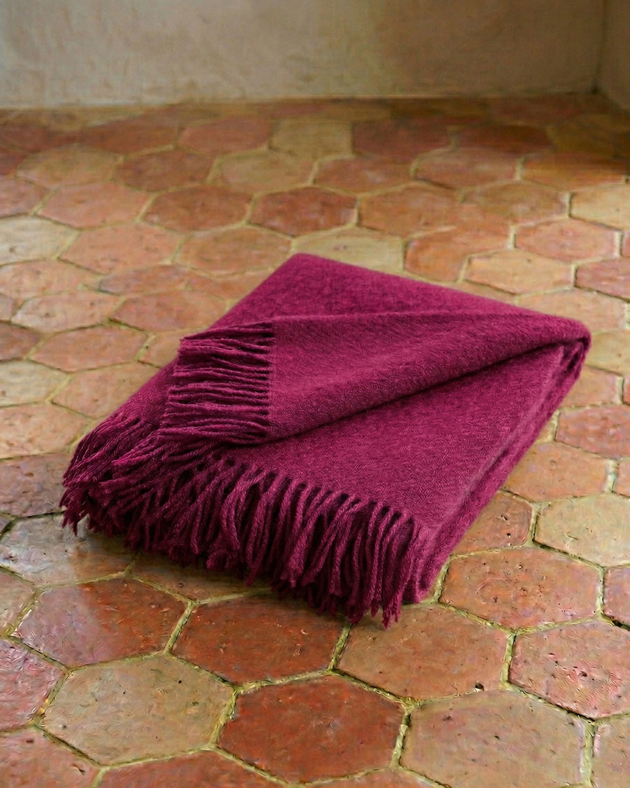Dark cerise blanket with fringes on a terracotta tiled floor. By Klippan, available via Wildschut Antiques.