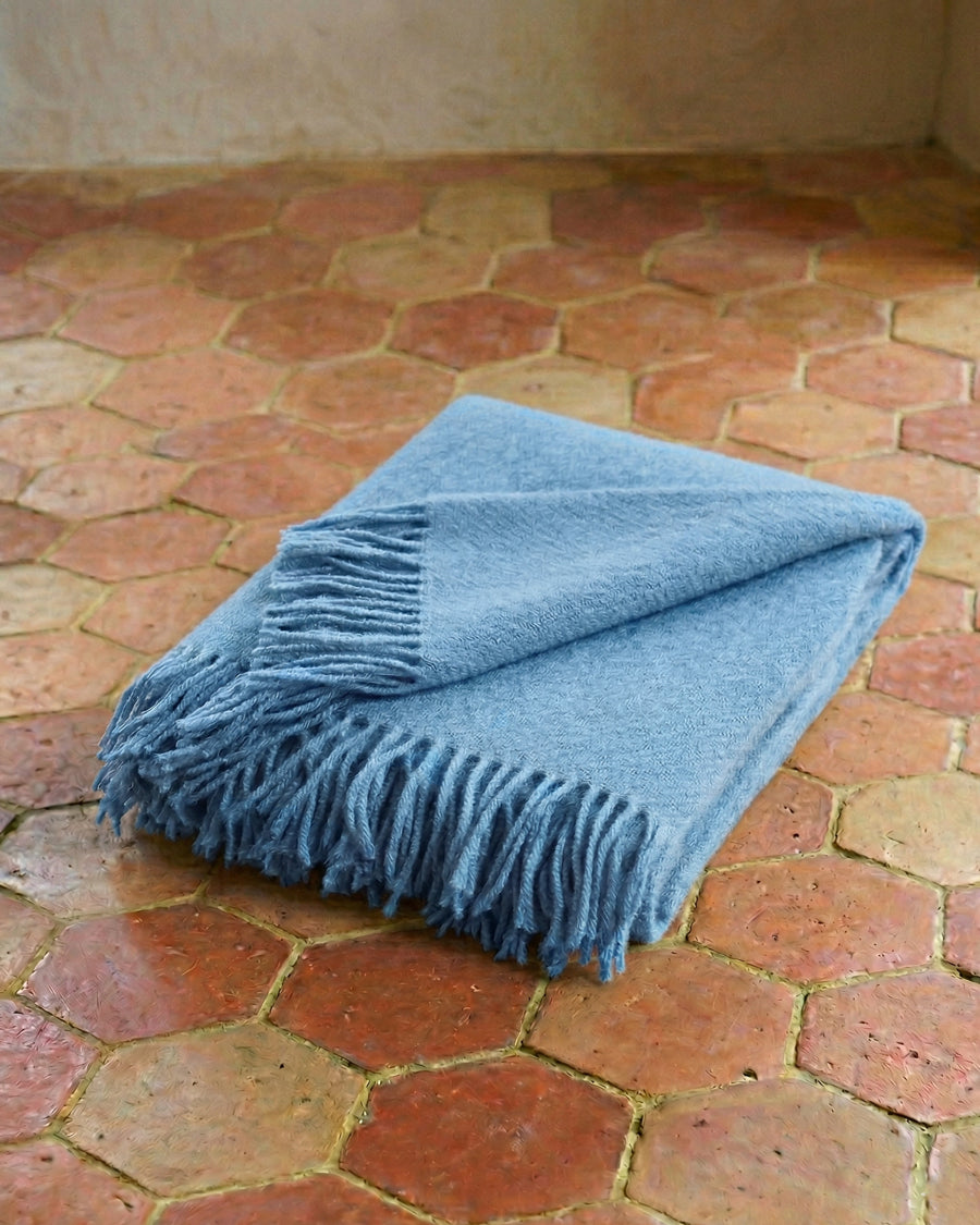 Light blue throw wool blanket with fringes on a terracotta tiled floor. By Klippan, available via Wildschut Antiques.