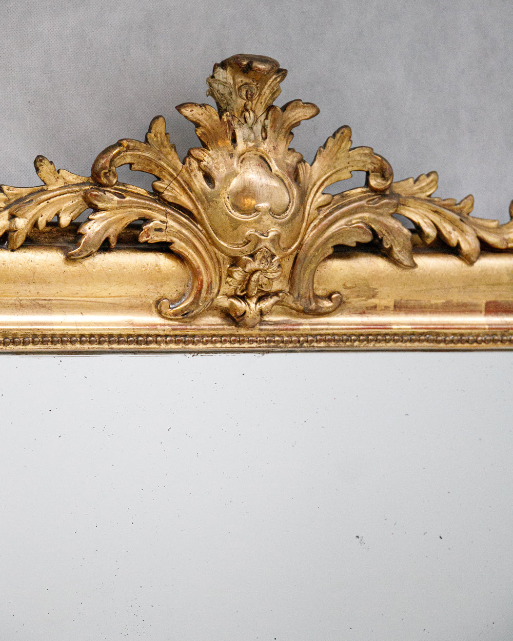 Close-up of a large antique French Louis Philippe mirror with a gilded frame and delicate floral crest, available at Wildschut Antiques
