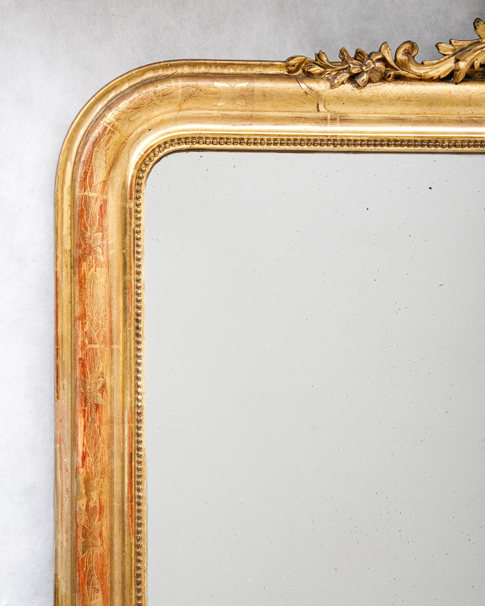 Close-up of a large antique French Louis Philippe mirror with a gilded frame and delicate floral crest