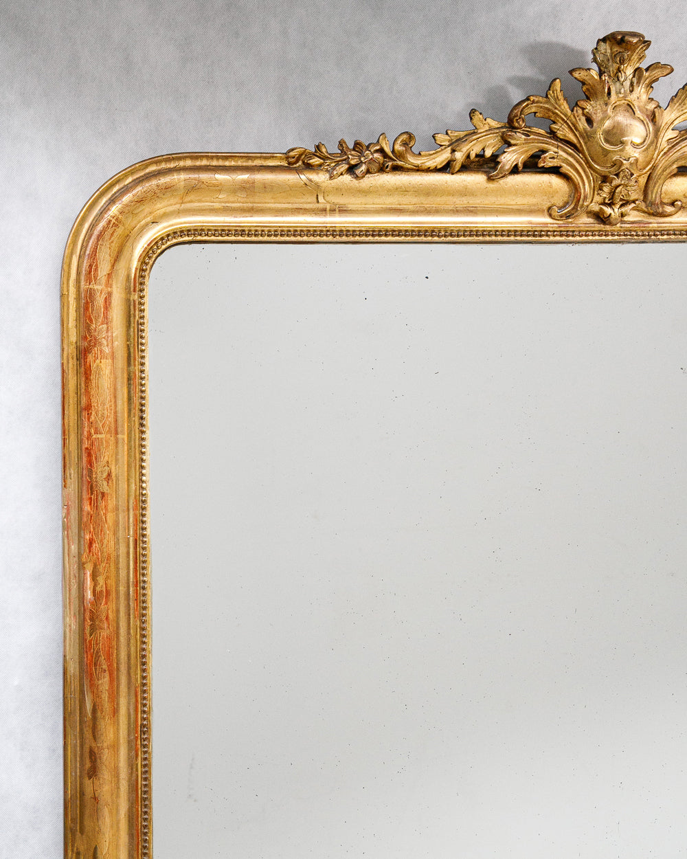 Close-up of a large antique French Louis Philippe mirror with a gilded frame and delicate floral crest