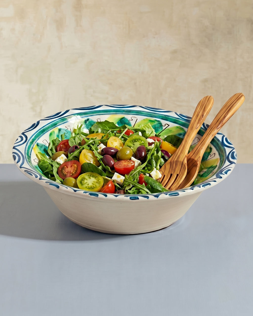 Colorful salad in a decorative bowl with wooden utensils on a neutral background