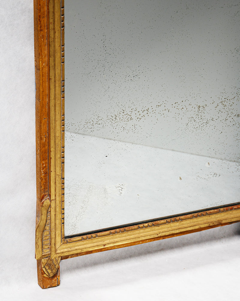 Close-up of the lower part of an antique French Louis XVI period giltwood trumeau marriage mirror, showing some foxing on the mirror glass.