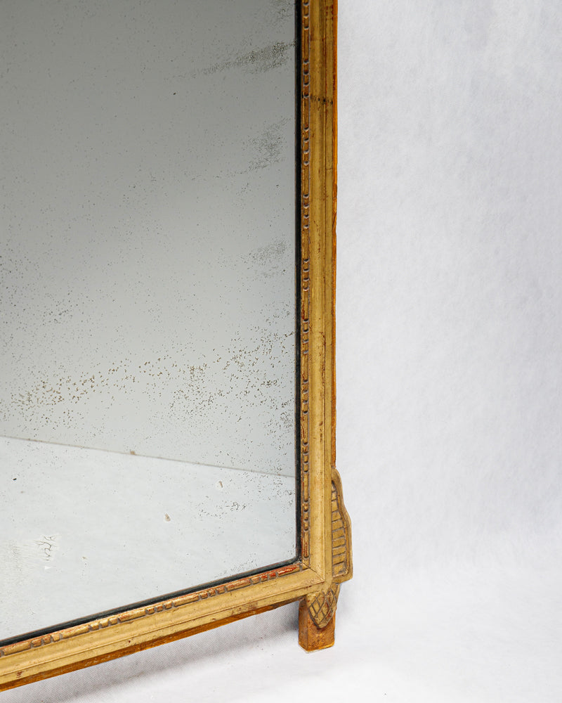 Close-up of the lower part of an antique French Louis XVI period giltwood trumeau marriage mirror, showing some foxing on the mirror glass.