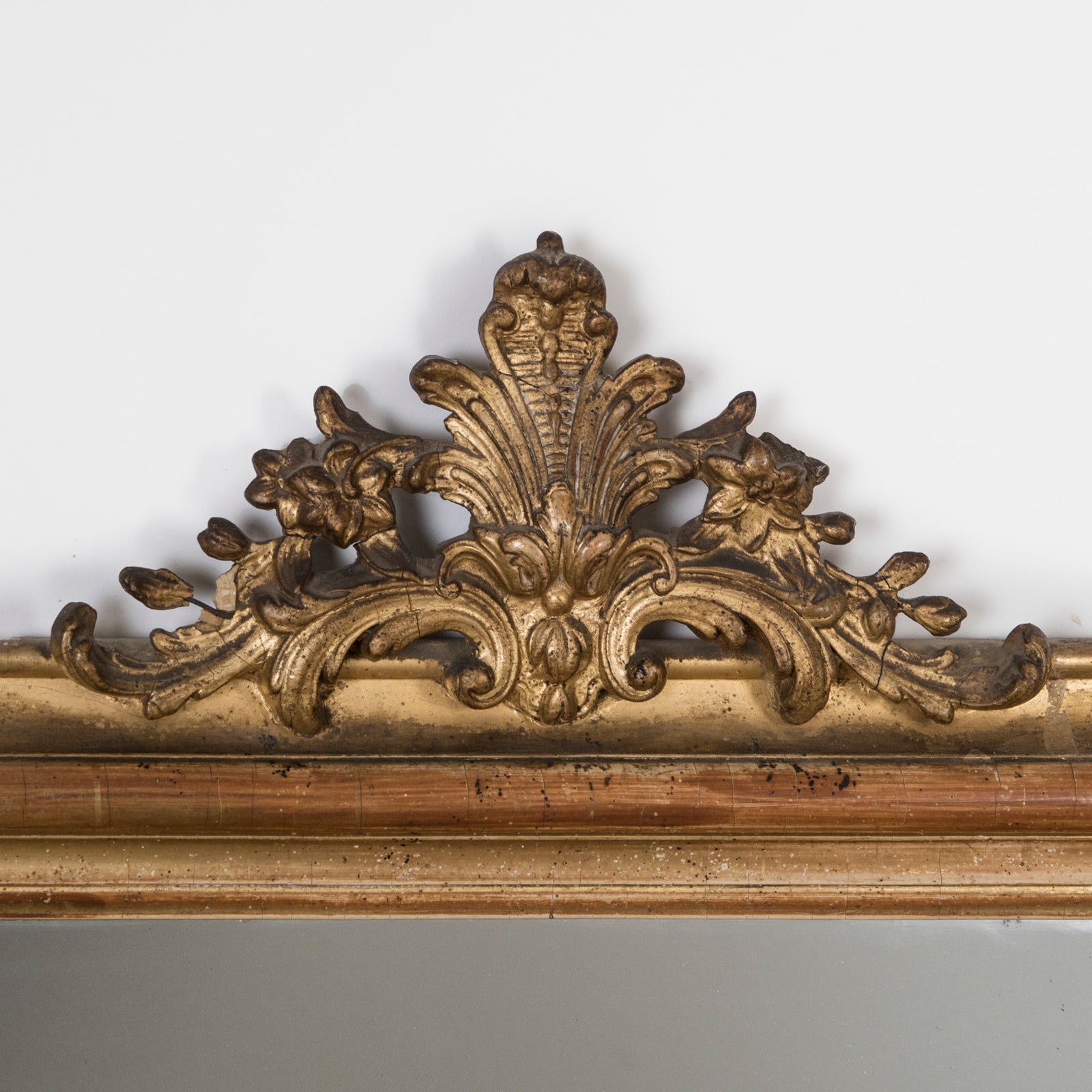 Close-up of the crest of an antique French 19th Century Louis Philippe style gold gilt mirror with small crest and rounded upper corners and some foxing on the glass