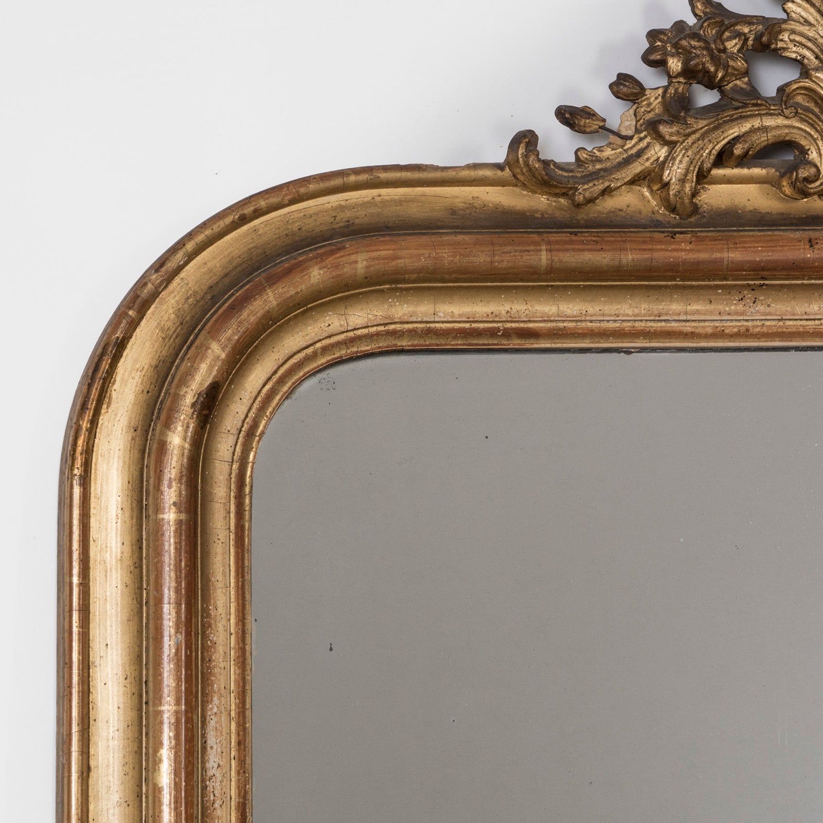 Close-up of an antique French 19th Century Louis Philippe style gold gilt mirror with small crest and rounded upper corners and some foxing on the glass