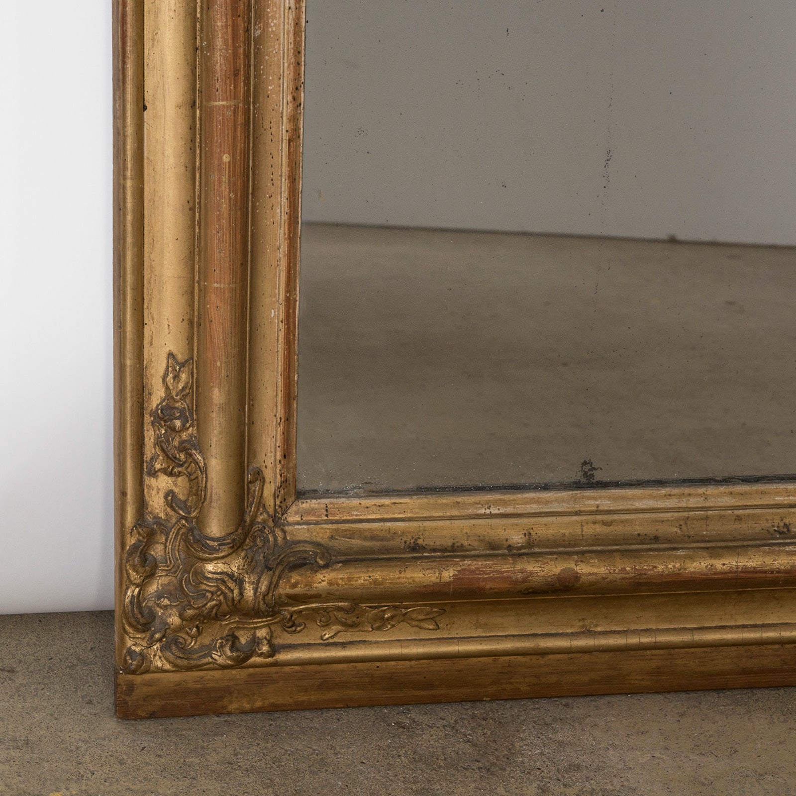 Close-up of the bottom part of an antique French 19th Century Louis Philippe style gold gilt mirror with small crest and rounded upper corners and some foxing on the glass