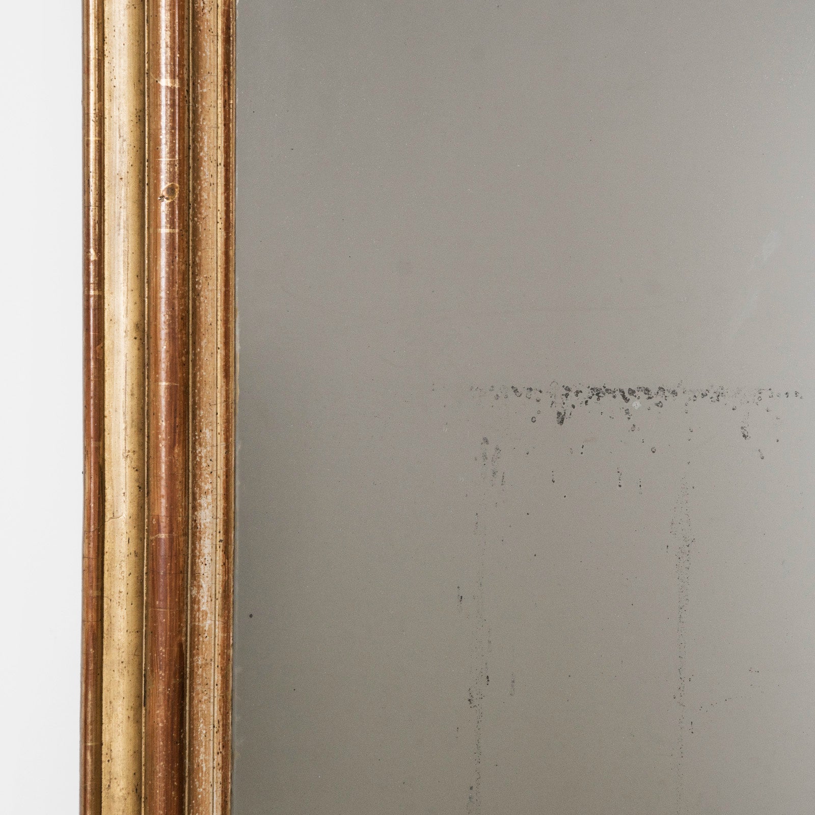 Close-up of the frame of an antique French 19th Century Louis Philippe style gold gilt mirror with small crest and rounded upper corners and some foxing on the glass