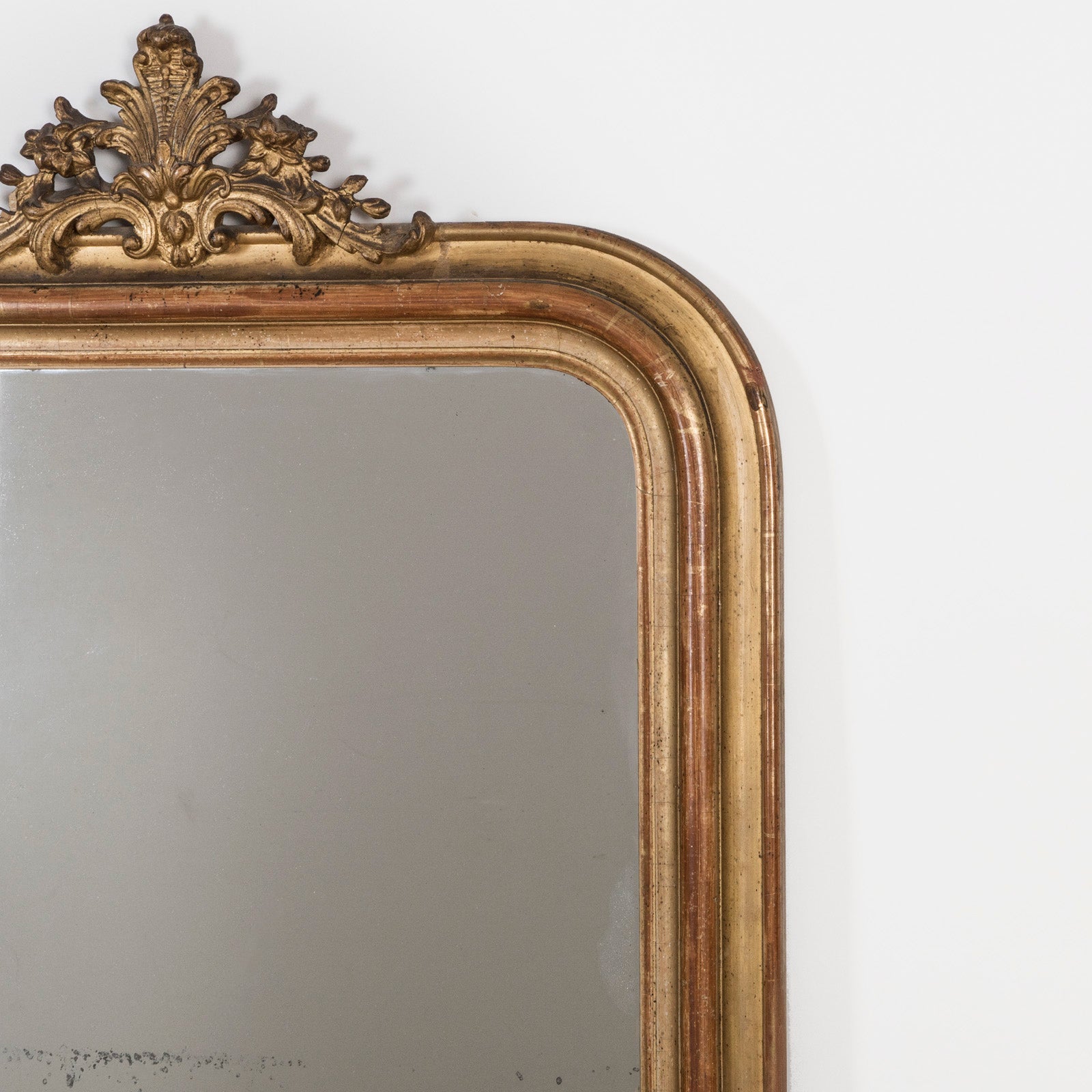 Close-up of an antique French 19th Century Louis Philippe style gold gilt mirror with small crest and rounded upper corners and some foxing on the glass