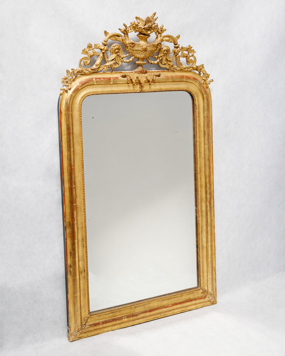 Antique French gold gilt mirror with a vase and flower crest, featuring a classic 'string of pearls' motif and hints of red bole, available at Wildschut Antiques