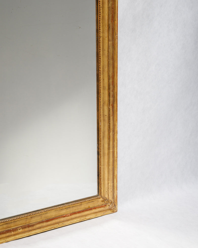 Detail of the frame of an antique French gold gilt mirror, featuring a classic 'string of pearls' motif and hints of red bole