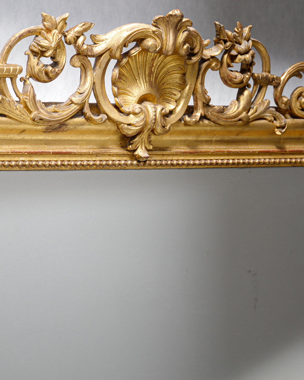 Close-up of an ornate shell and floral crest ornament of an antique French gold gilt mirror from Wildschut Antiques
