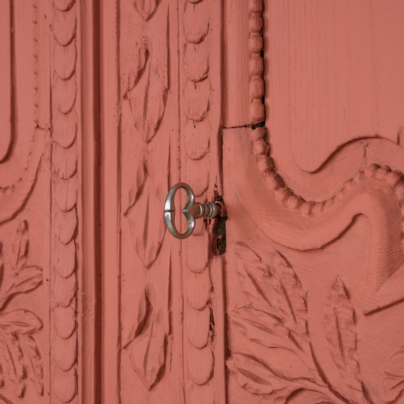 Detail of the doors and key of an antique French marriage armoire, painted in vibrant brick red.
