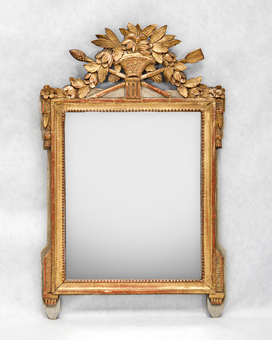 A French Louis XVI period giltwood trumeau mirror with a finely carved crest featuring a flower-filled basket, laurel leaf garlands, tassels, and delicate pearl beading, available at Wildschut Antiques