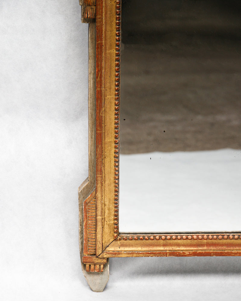 Corner detail of an antique French Louis XVI period giltwood trumeau mirror with a finely carved crest featuring a flower-filled basket, laurel leaf garlands, and delicate pearl beading
