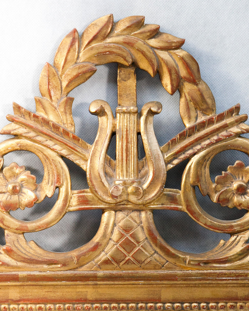 Decorative gold crest emblem with musical lyre and laurel wreath on a gray background. The crest of an antique mirror.