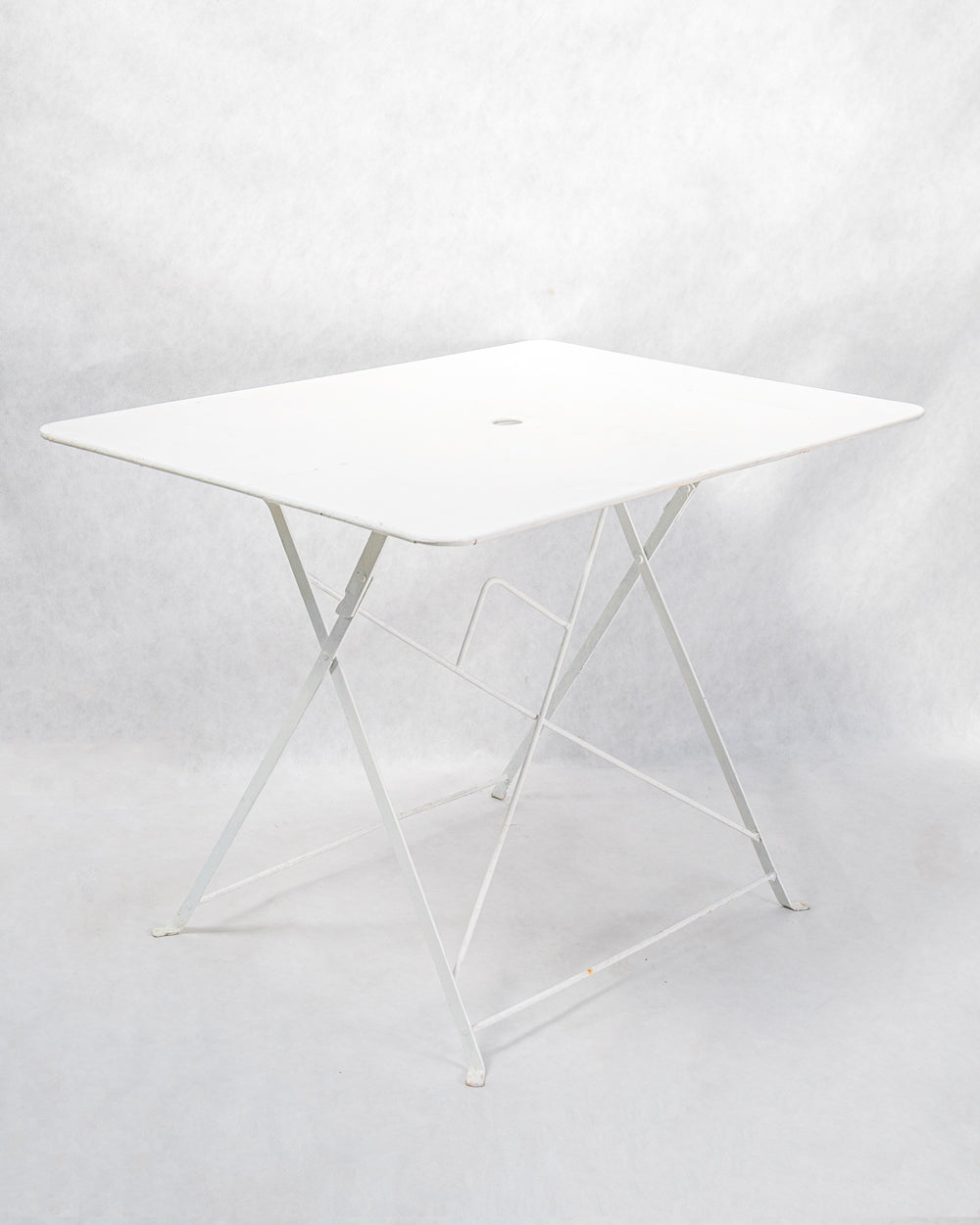 Sideview of a vintage French white rectangular metal folding garden table with a collapsible frame.