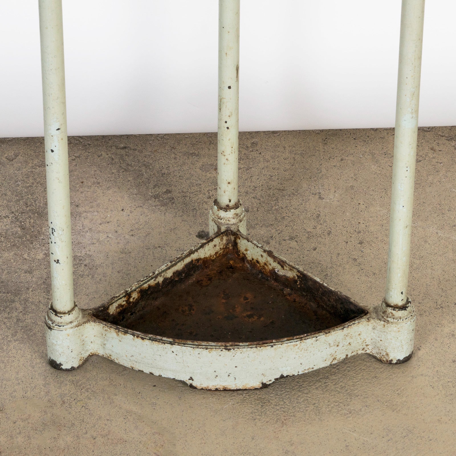 Close-up of the bottom part of an antique mint green brass and painted iron corner umbrella rack with aged patina
