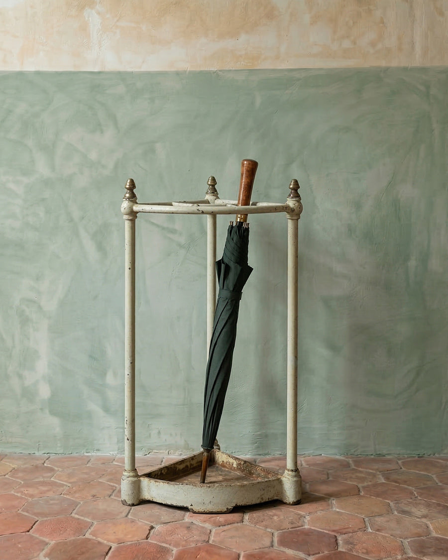Antique French umbrella stand with a dark green umbrella against a textured wall.