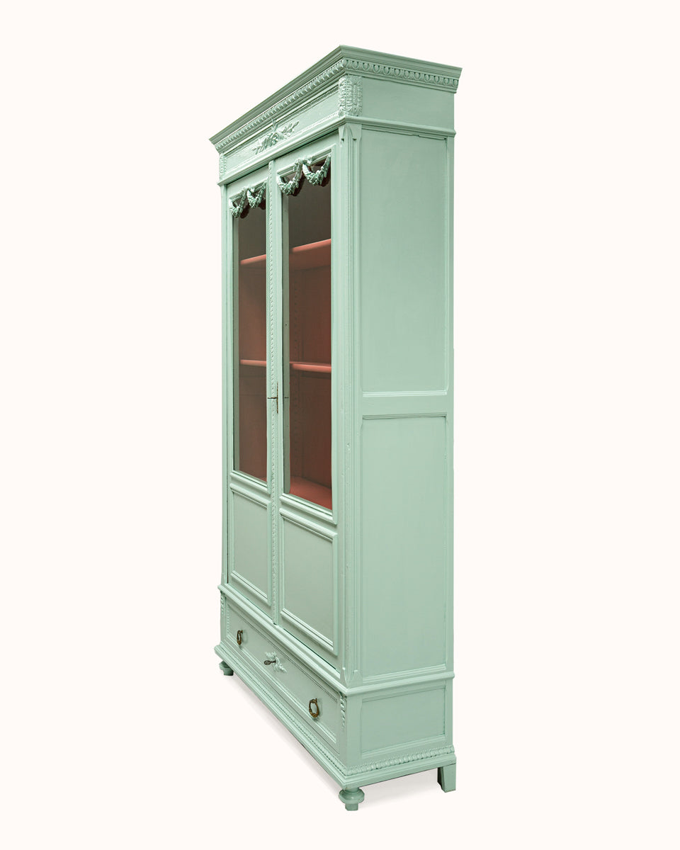 Sideview of a French Louis XVI-style vitrine cabinet with a soft mint green finish, glass doors, and contrasting red interior, intricate detailing.