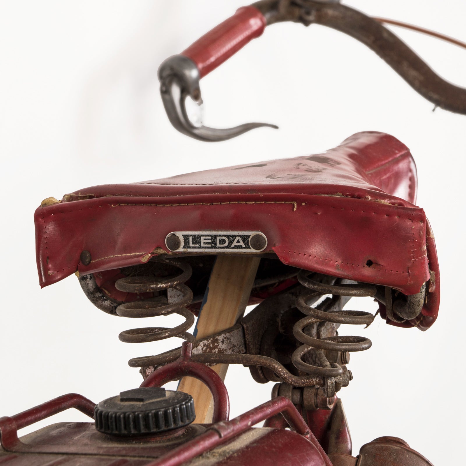 Close-up of the sadle of a vintage French Mobylette motorcycle, type Mosquito, with a red body and red seat, featuring a great patina finish and original mechanisms