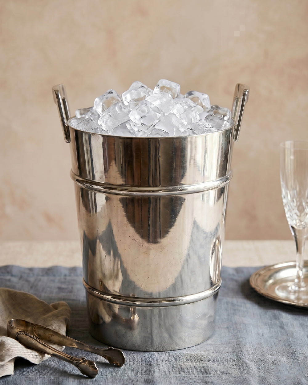 Vintage silver plated Modernist style ice bucket with ice cubes on a table with a neutral background. Available at Wildschut Antiques.
