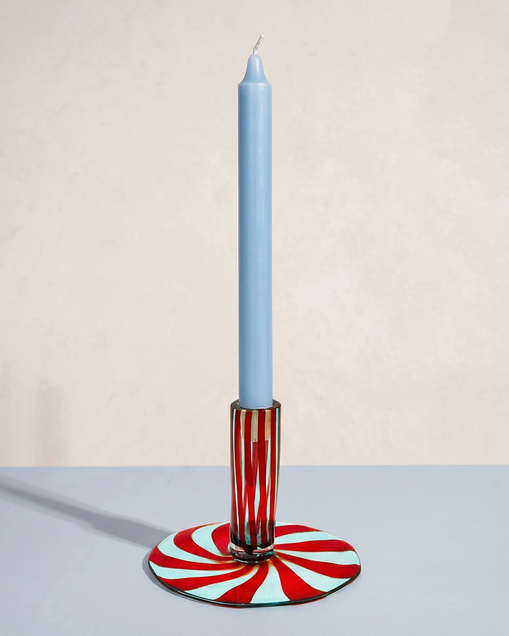 Candle holder with a red and light blue striped Murano Glass base holding a blue candle on a neutral background. Available at Wildschut Antiques.