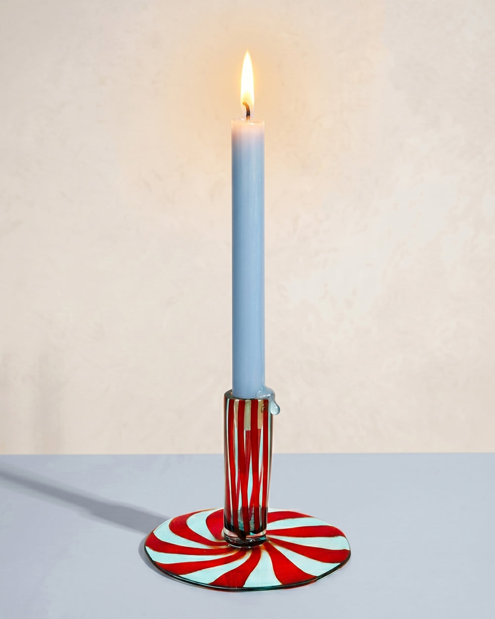 Murano glass candle holder with red and pale blue striped base, topped with a light blue burning candle, styled against a neutral background. Decorative Italian glassware available at Wildschut Antiques.