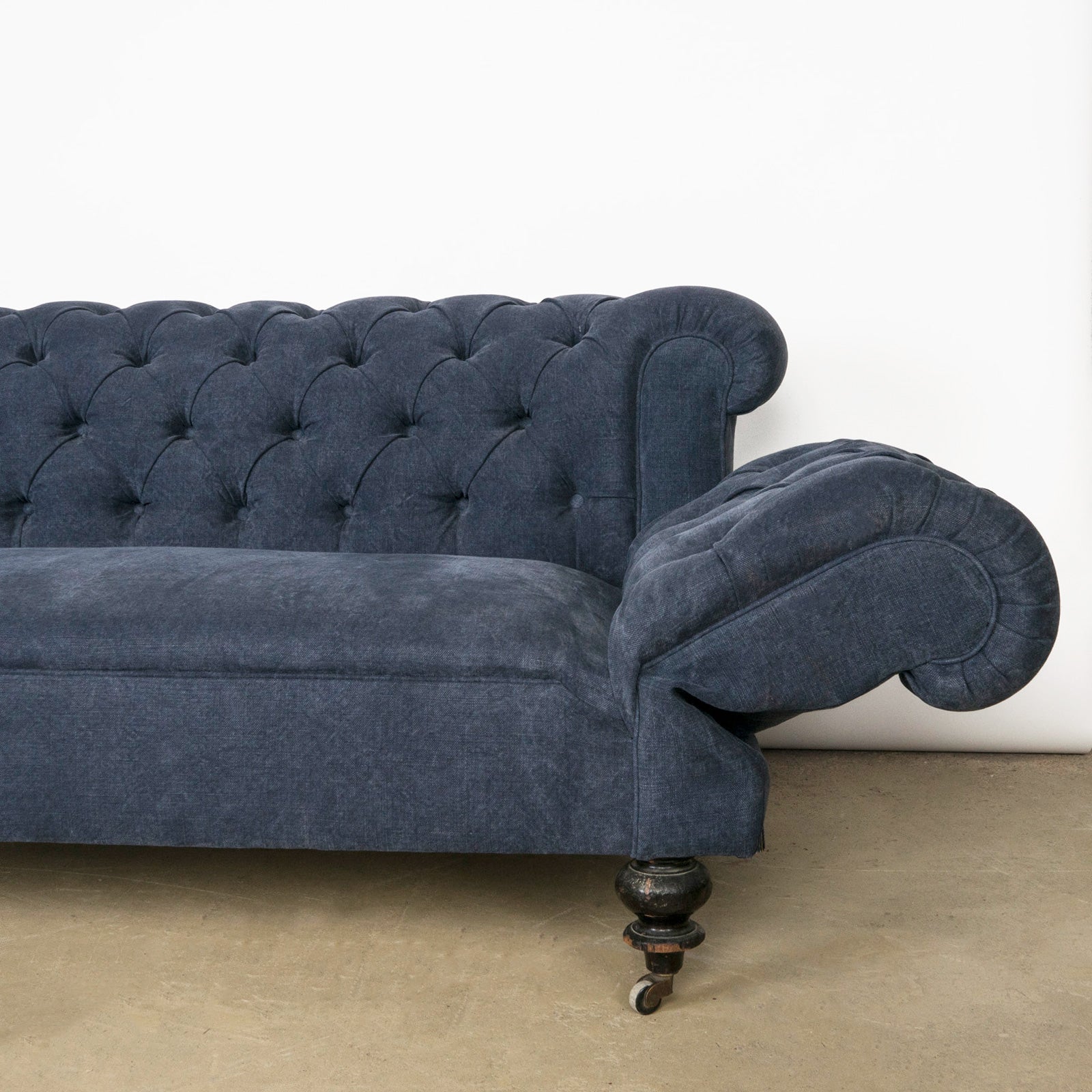 Close-up of the drop-end detail on an elegantly tufted 19th-century French Napoleon III sofa, upholstered in stonewashed blue linen—available at Wildschut Antiques.