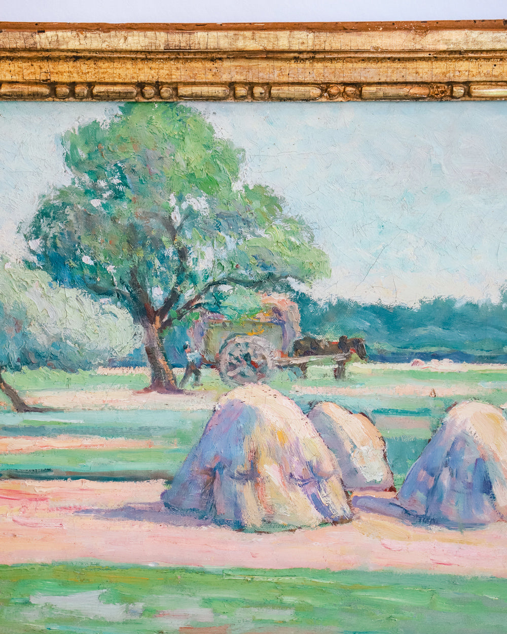 Close-up of a vibrant antique French painting showing a field with haystacks and distant figures at work, set in a giltwood frame.