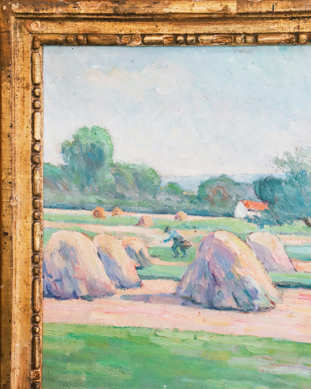 Close-up of a vibrant antique French painting showing a field with haystacks and distant figures at work, set in a giltwood frame.