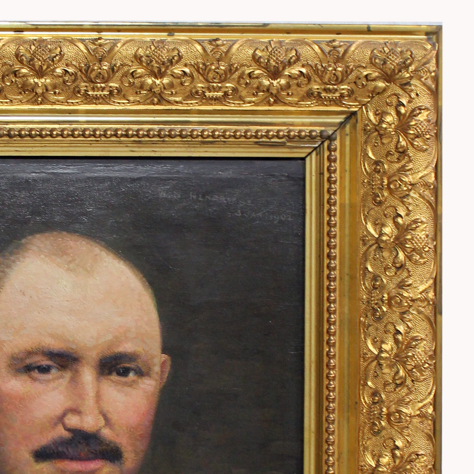 Close-up of an antique oil portrait of a gentleman with a moustache, bald head, and dark suit, in a giltwood frame