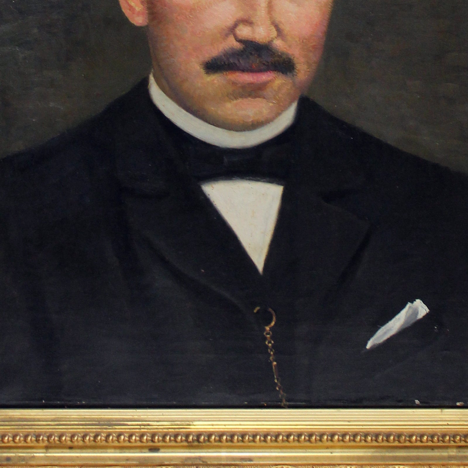 Close-up of an antique oil portrait of a gentleman with a moustache, bald head, and dark suit, in a giltwood frame
