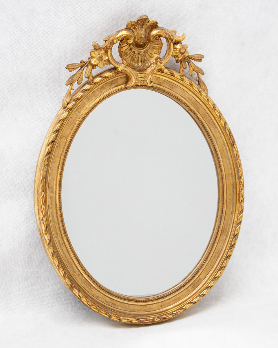 Decorative antique French gold-framed oval mirror on a white background