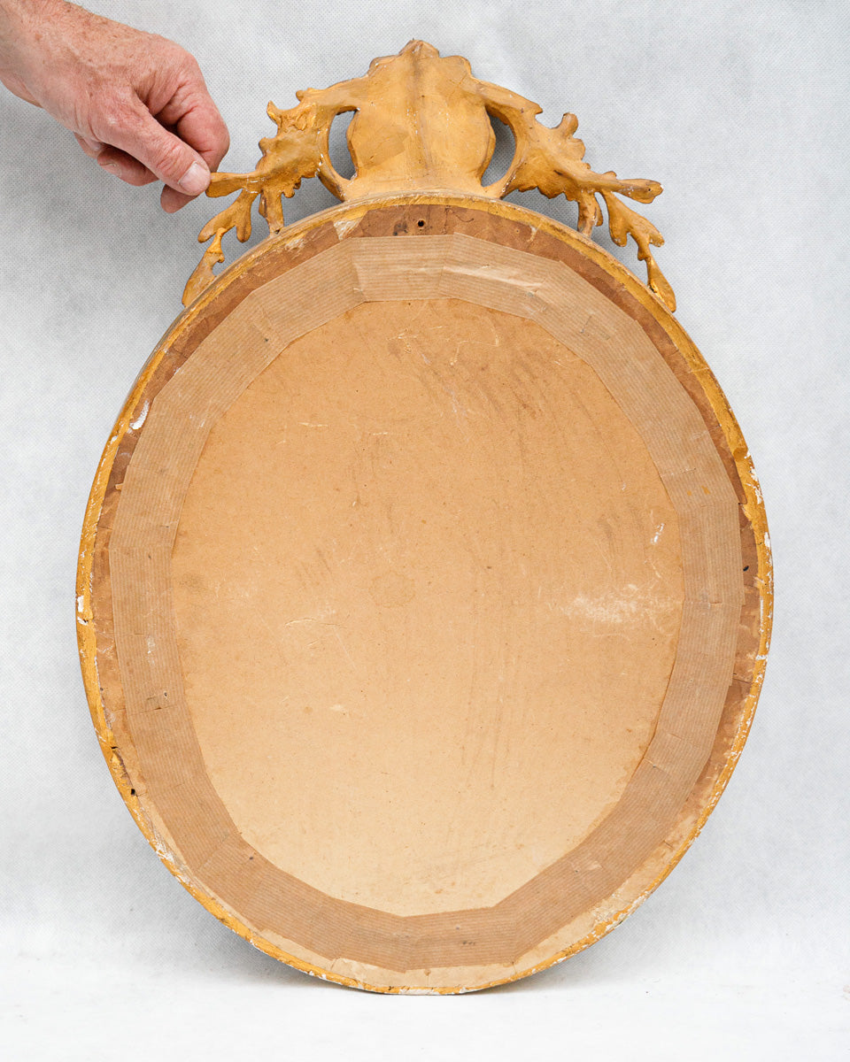 Wooden backside of an antique oval mirror held by a hand on a light gray background