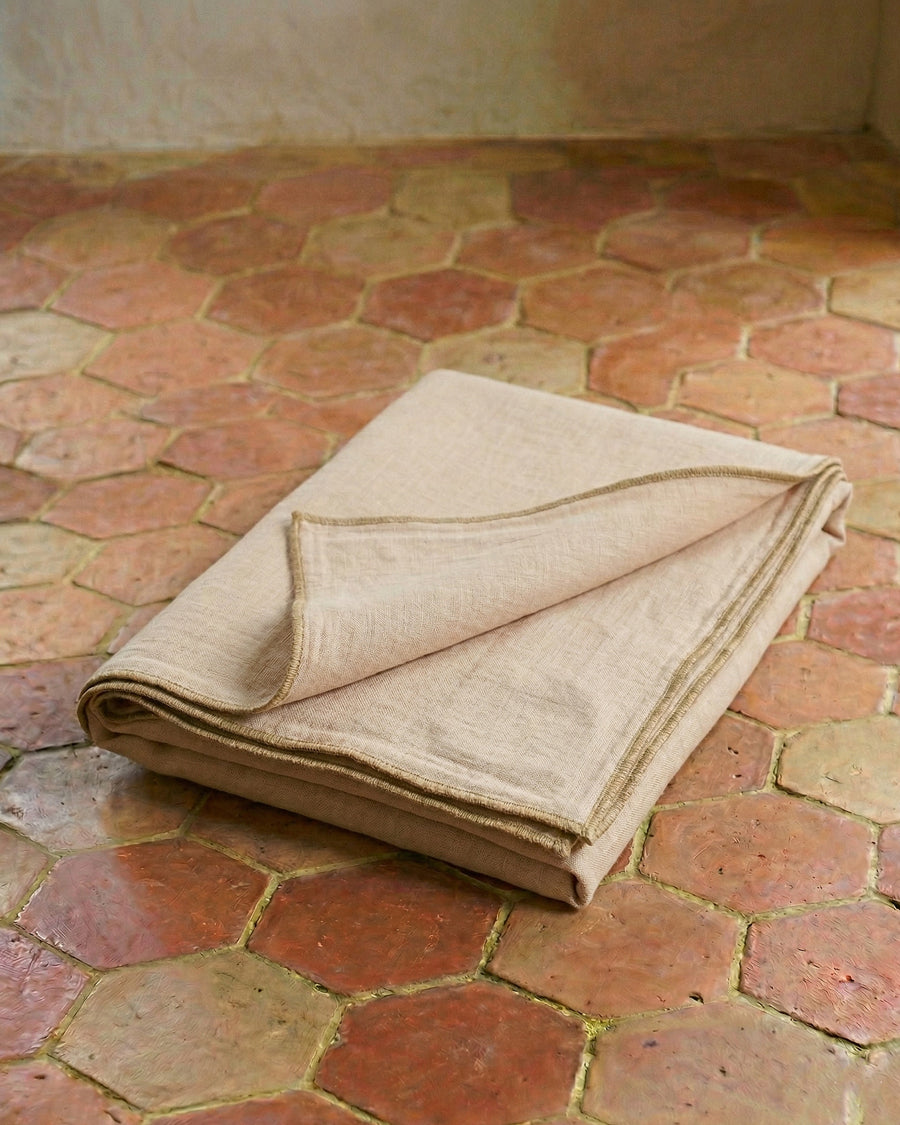 Folded soft pink linen throw on a terracotta-tiled floor, available via Wildschut Antiques.
