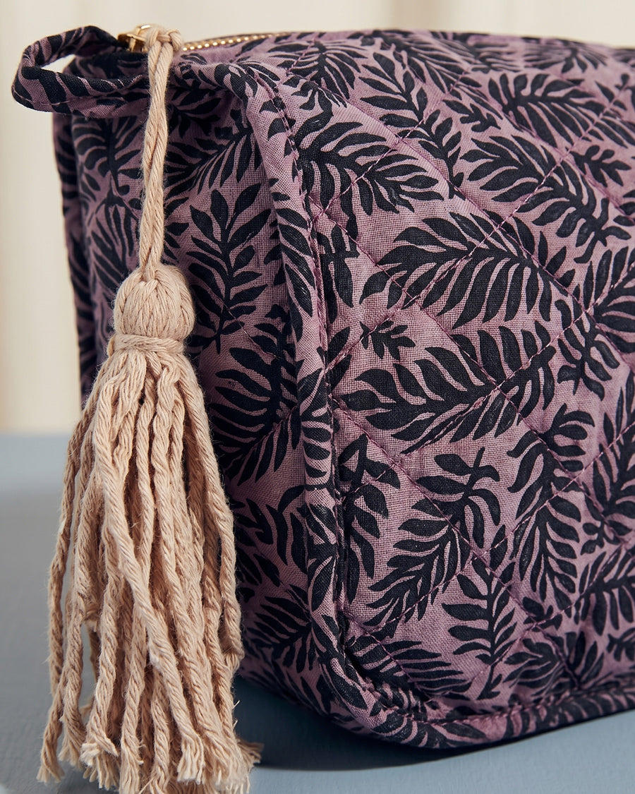 Purple pouch with black leaf pattern and beige tassel on a light gray background