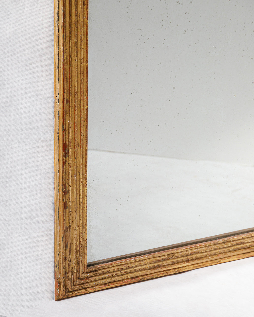 Close-up of a small antique French rectangular mirror with a striped gold frame with some foxing on the mirror glass on a plain background