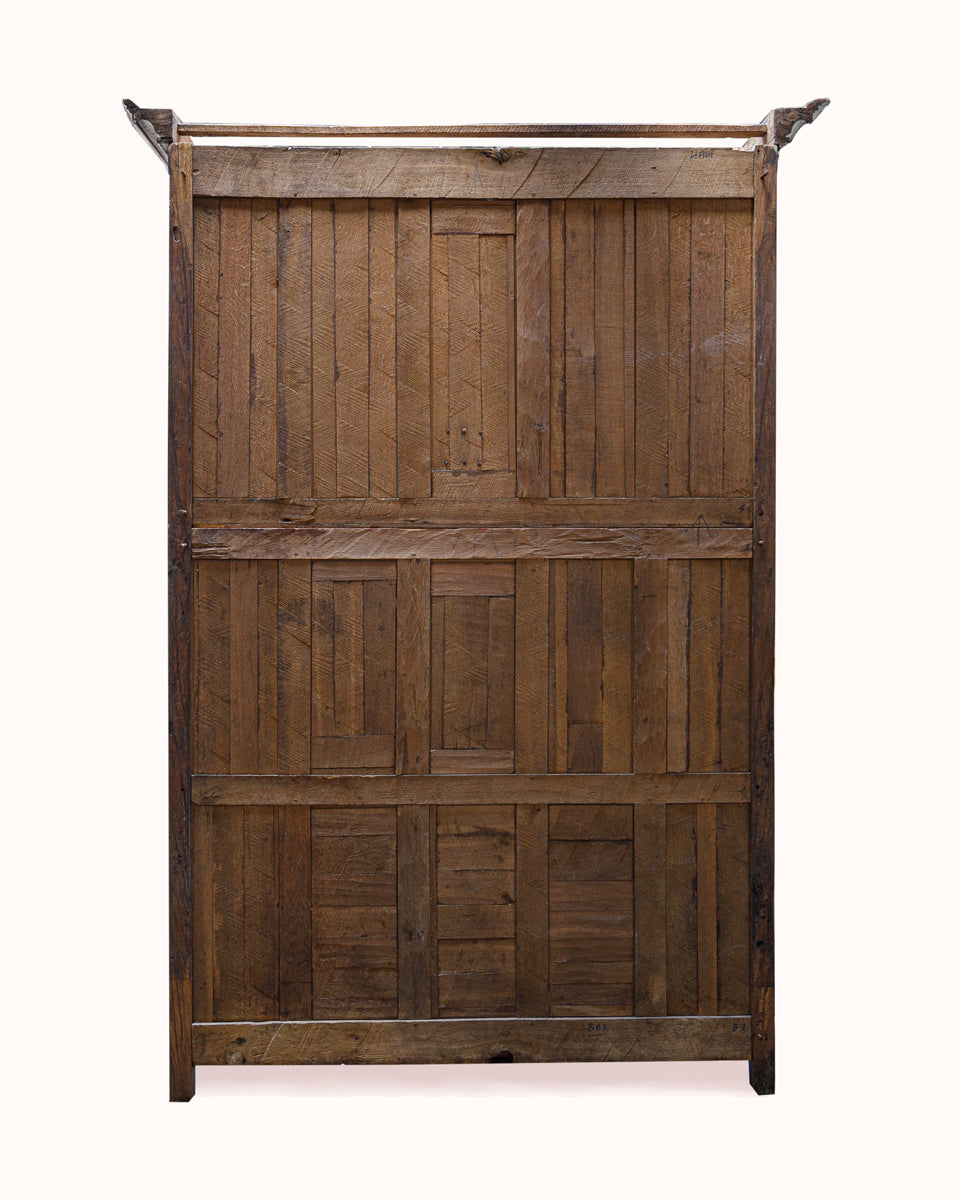 The backside of an antique French wooden wardrobe with a rustic design on a plain background