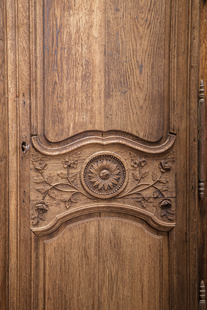 Close-up of a wooden door of a antique French marriage armoire or wardrobe with intricate carvings.
