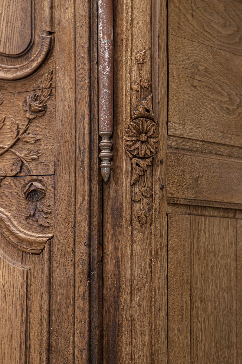 Close-up of one of the hinges and a wooden door with intricate carvings and floral designs belonging to a French antique marriage armoire or wardrobe