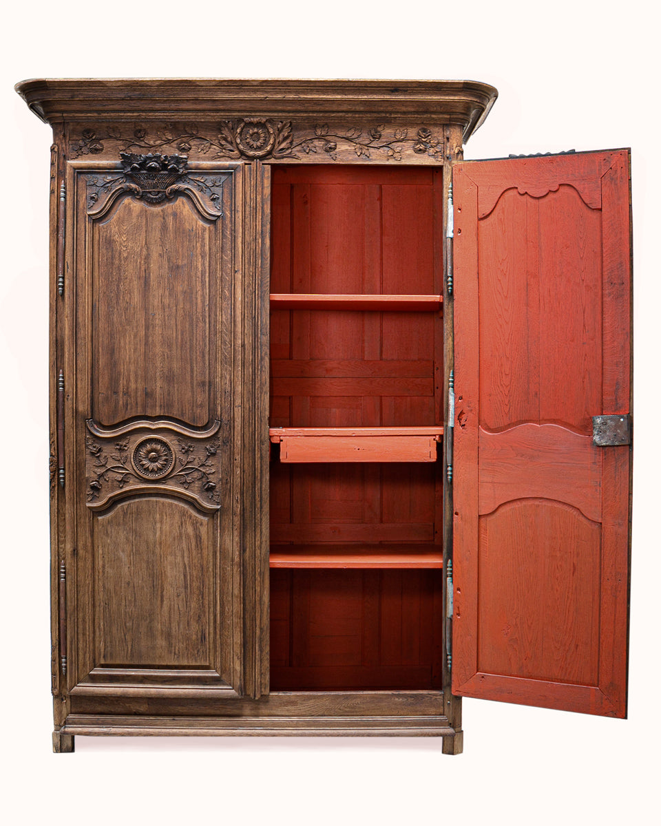 The interior of an antique French wooden armoire or marriage wardrobe featuring intricate carvings, shown against a white background.