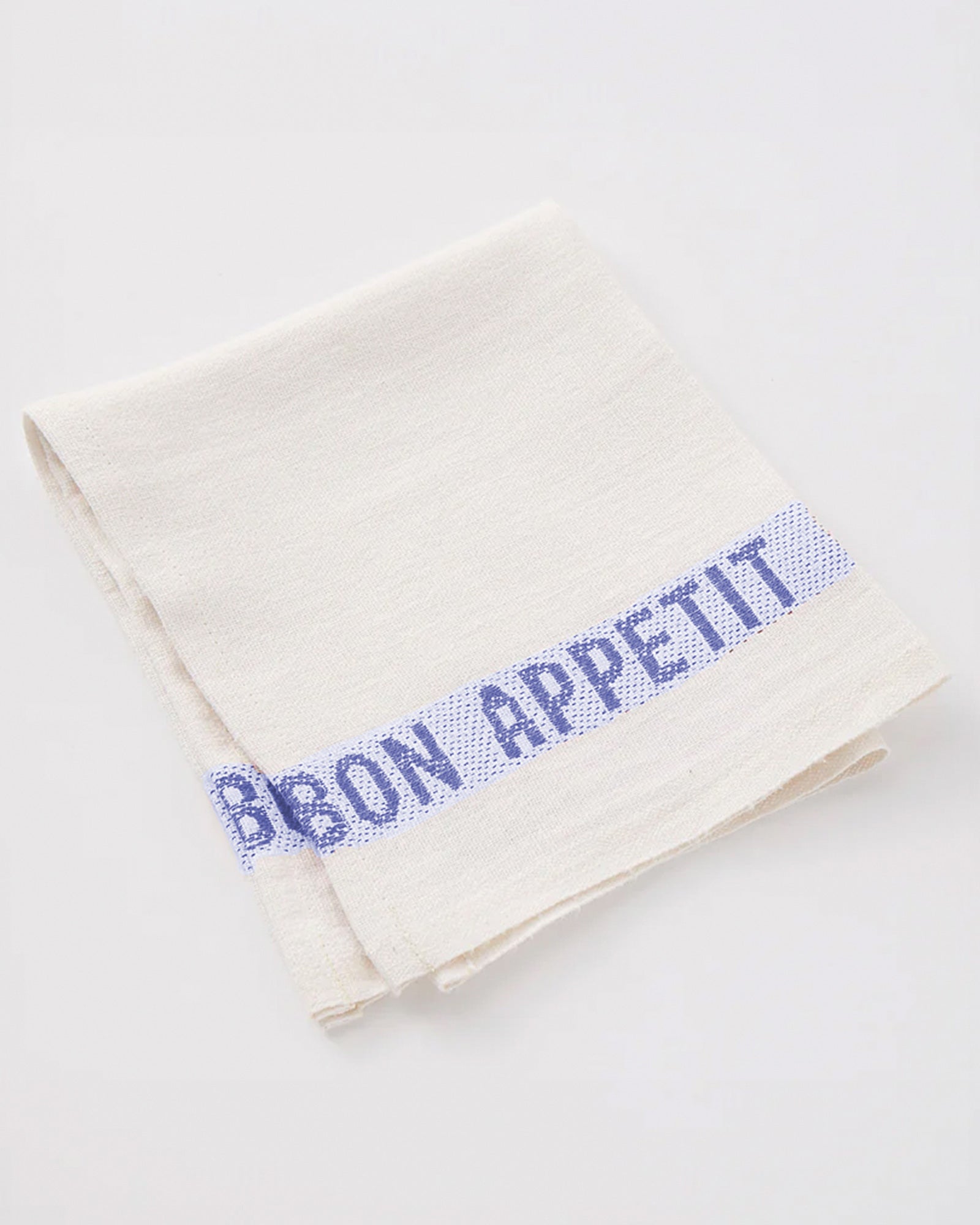 A crisp white linen napkin with 'Bon Appétit' embroidered along the edges in blue by Charvet Editions available at Wildschut Antiques