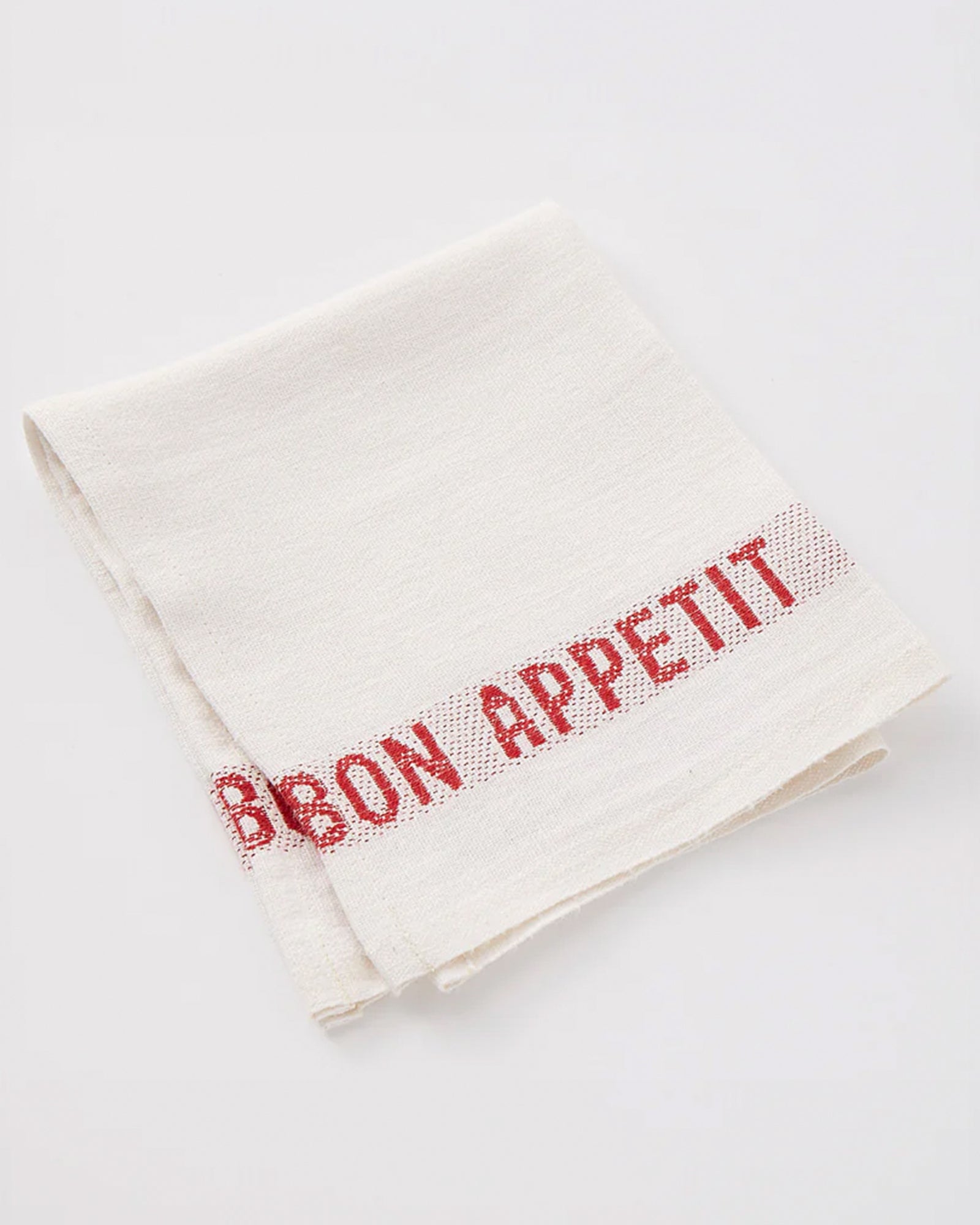 A crisp white linen napkin with 'Bon Appétit' embroidered along the edges in red by Charvet Editions available at Wildschut Antiques