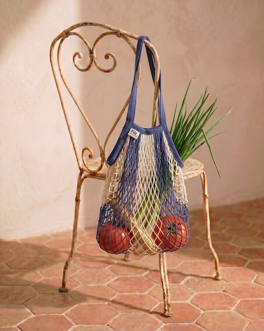 Net shopping bag with fruits on a decorative vintage metal chair against a beige wall. By Filt 1860, available at Wildschut Antiques.
