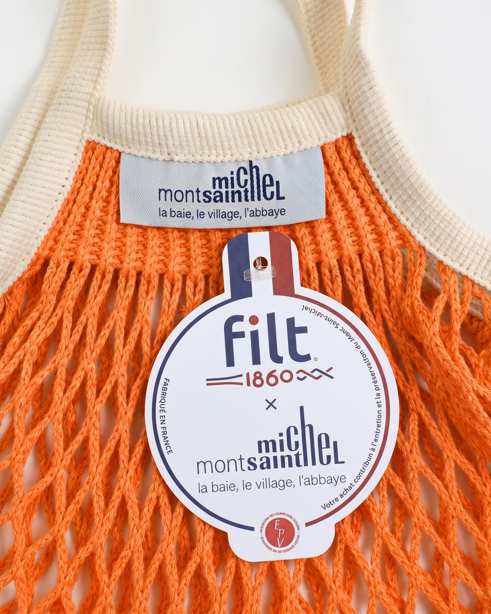 Close-up of a orange net shopping bag with ecru handles and visible brand label by Filt 1860 on a white background. Available at Wildschut Antiques.