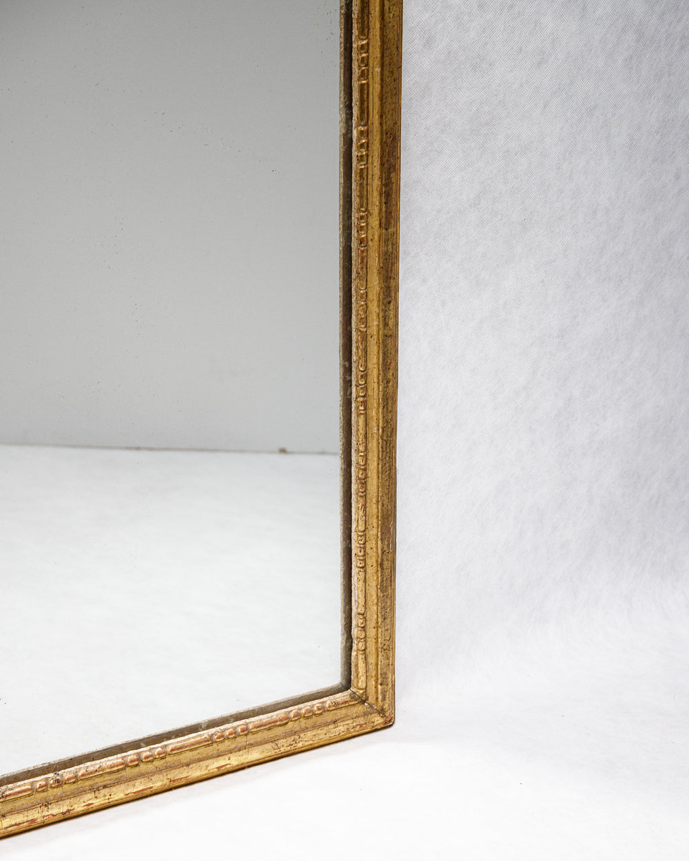 Close-up of a 19th-century French Louis XVI style giltwood mirror with a rectangular frame, decorated with gesso and gold leaf finish