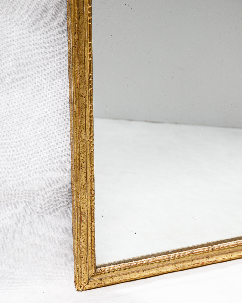 Close-up of a 19th-century French Louis XVI style giltwood mirror with a rectangular frame, decorated with gesso and gold leaf finish