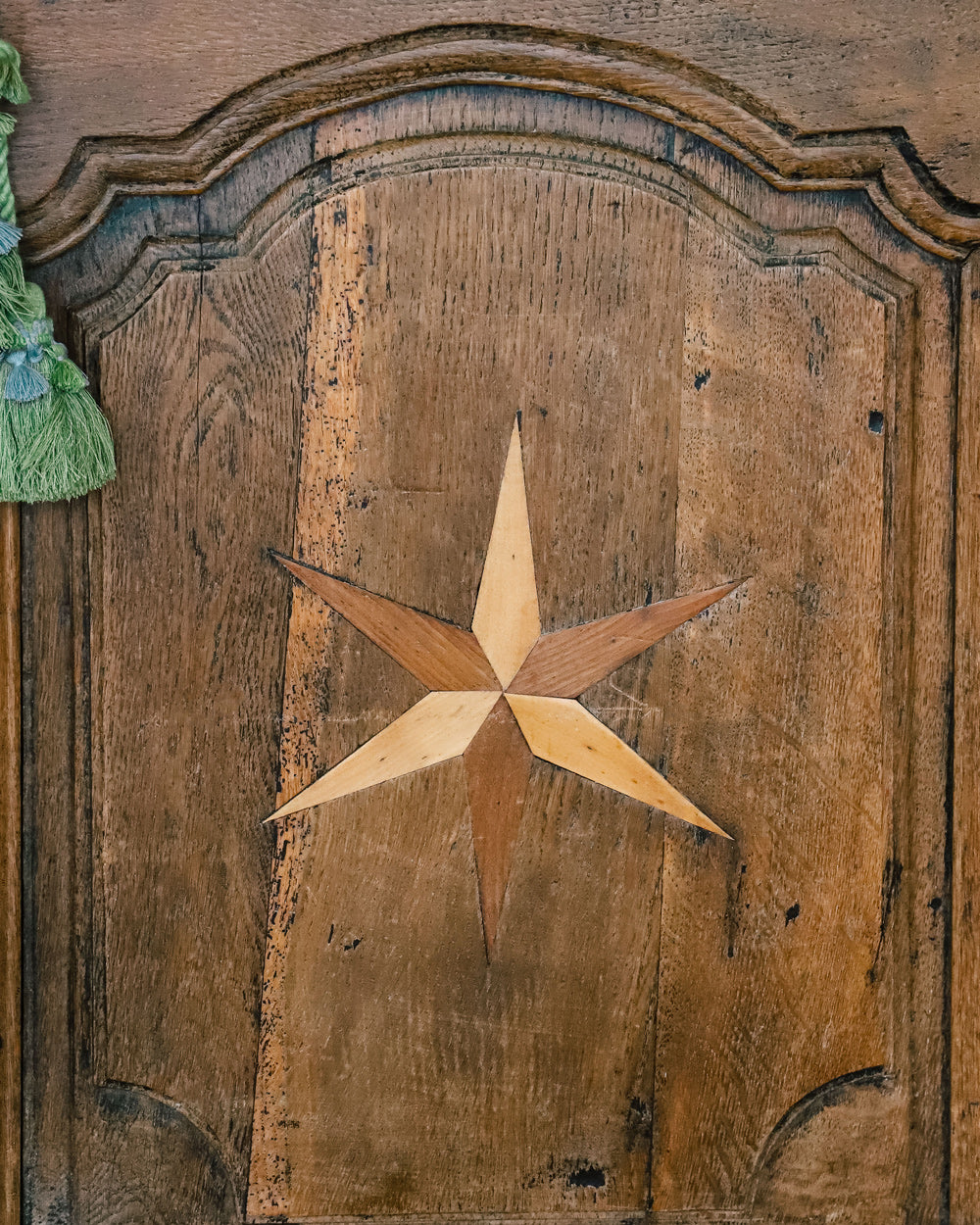 Close-up of a door panel of an antique French Louis XV style armoire with star shaped inlays on the doors, made of wood with a visible rustic finish