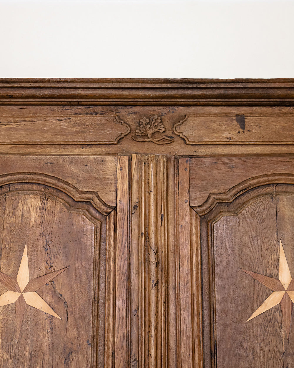 Detail of the top part of an antique French Louis XV style armoire with star shaped inlays on the doors, made of wood with a visible rustic finish